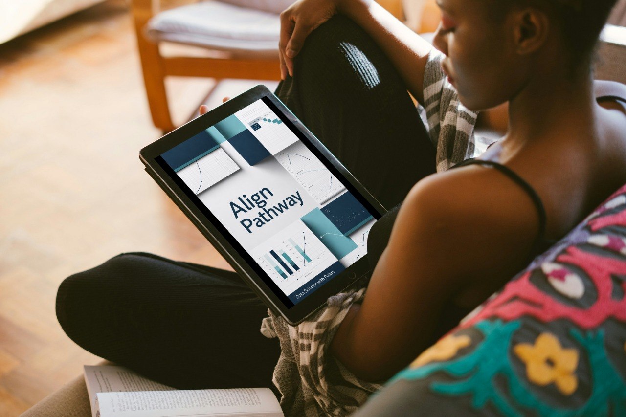 A person sitting indoors holds a tablet displaying a presentation titled 'Axis Pack' with geometric charts and graphs. The scene includes a wooden chair in the background and a colorful patterned cushion in the foreground.