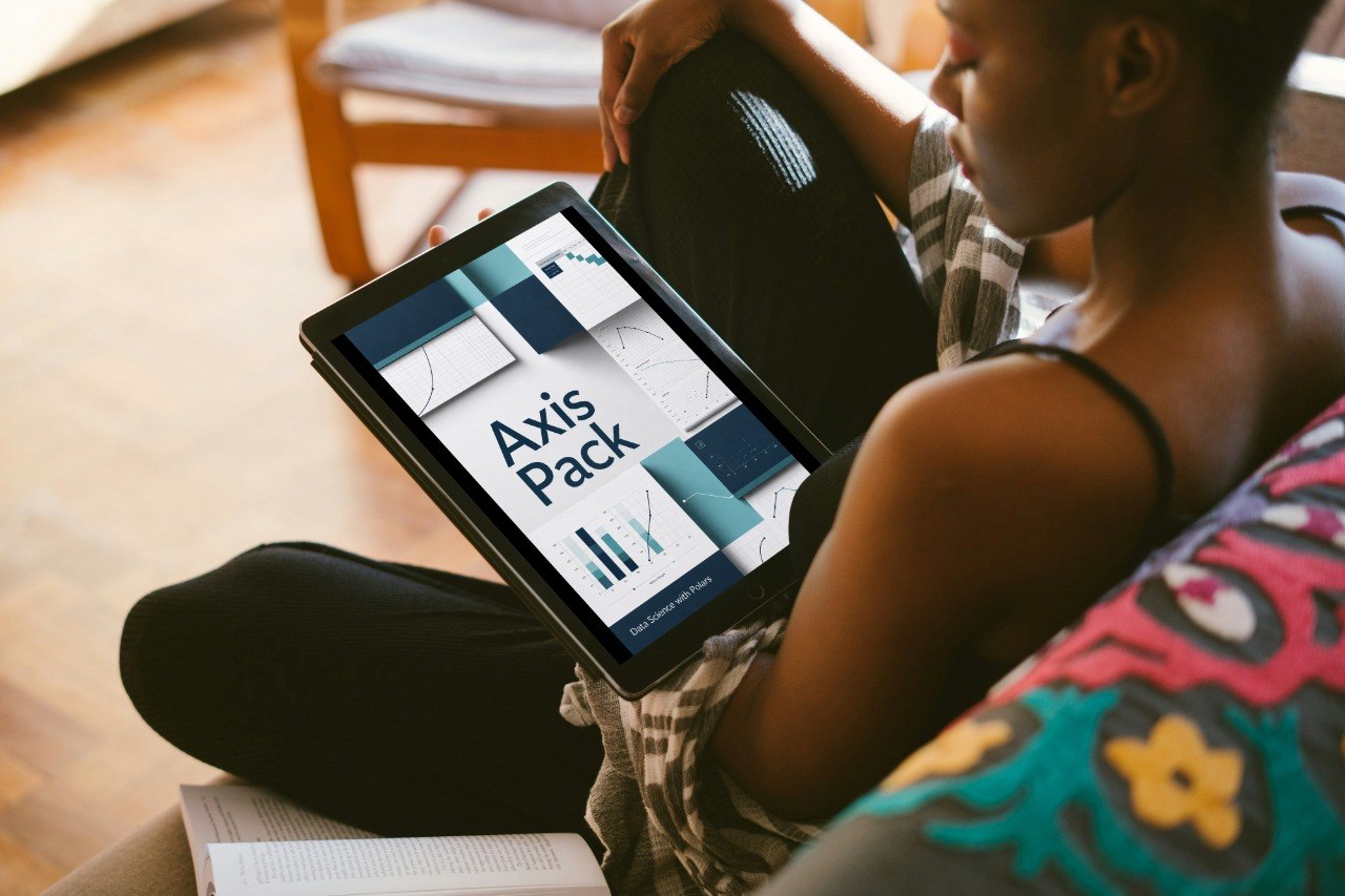 A person sitting indoors holds a tablet displaying a presentation titled 'Axis Pack' with geometric charts and graphs. The scene includes a wooden chair in the background and a colorful patterned cushion in the foreground.