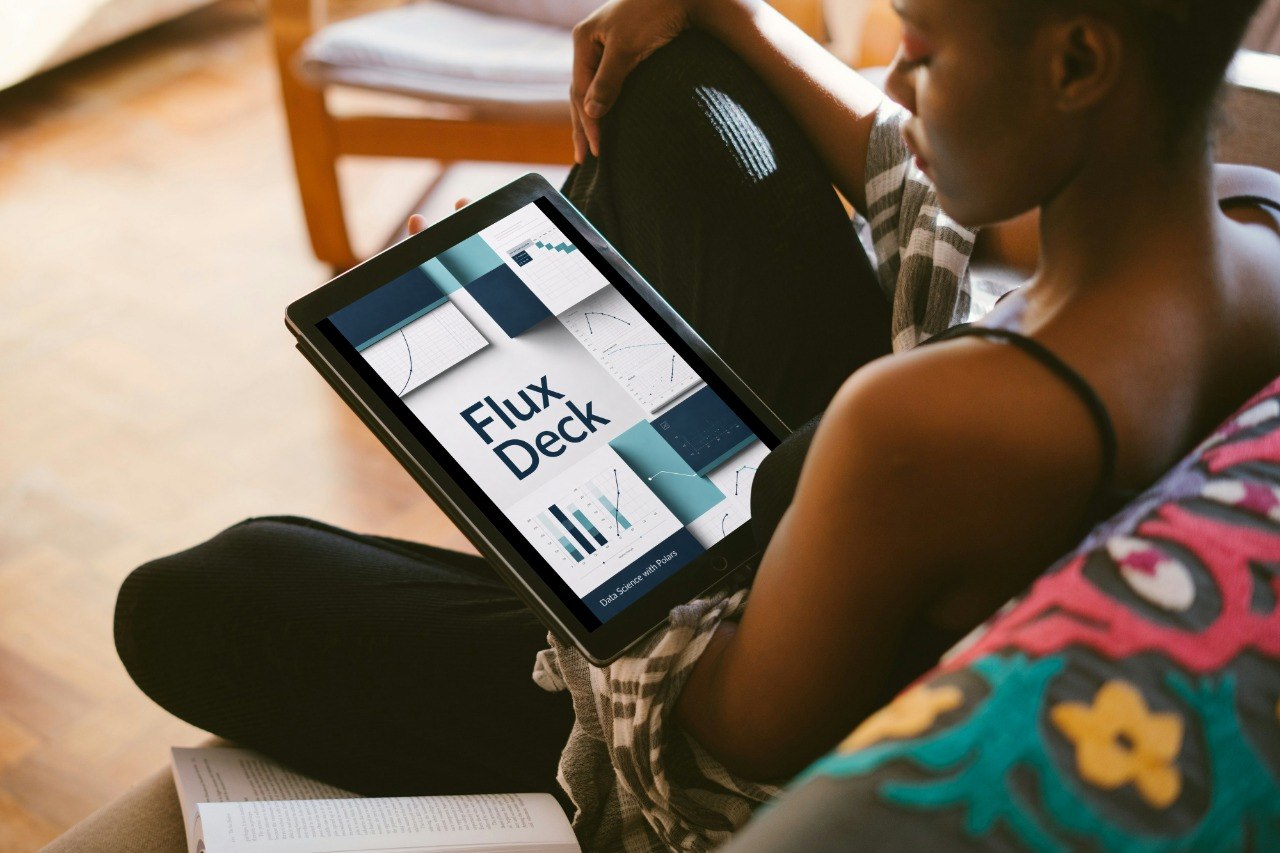 A person sitting indoors holds a tablet displaying a presentation titled 'Axis Pack' with geometric charts and graphs. The scene includes a wooden chair in the background and a colorful patterned cushion in the foreground.