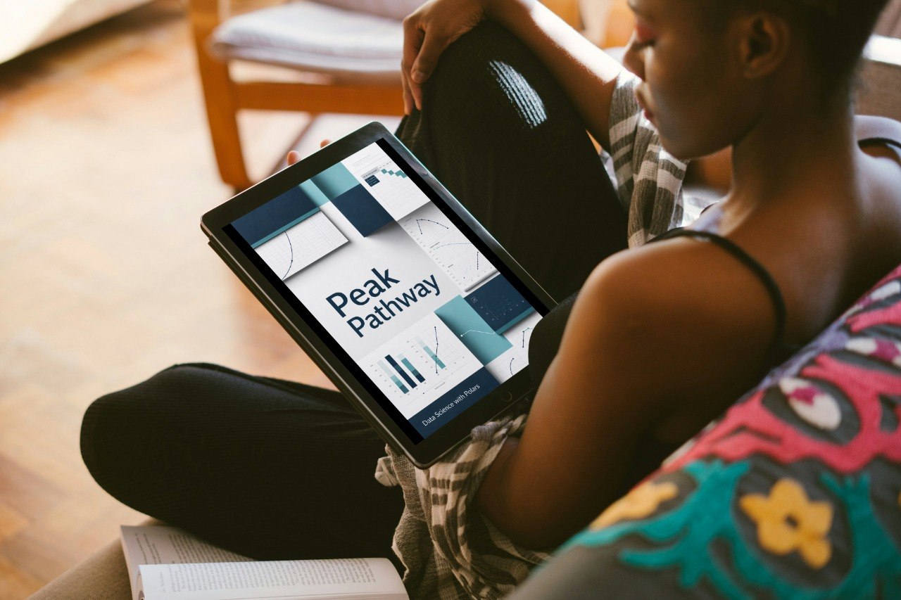 A person sitting indoors holds a tablet displaying a presentation titled 'Axis Pack' with geometric charts and graphs. The scene includes a wooden chair in the background and a colorful patterned cushion in the foreground.